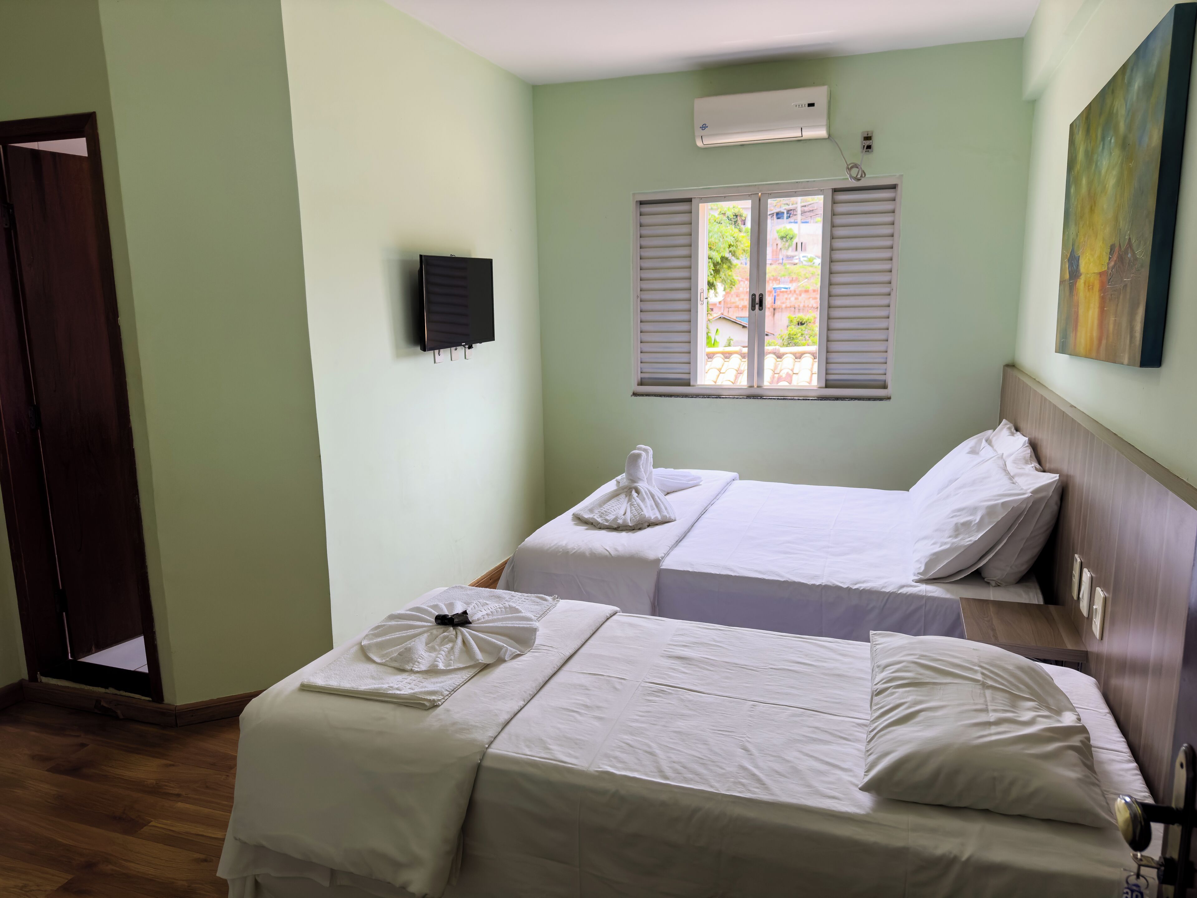 Habitació d'hotel amb dos llits, una finestra amb persianes, un aire condicionat i un quadre a la paret.