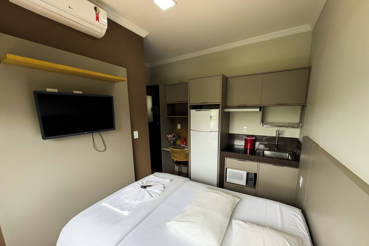 Une chambre d’hôtel équipée d’un lit, d’une télévision, d’une kitchenette et d’un téléviseur à écran plat fixé au mur.