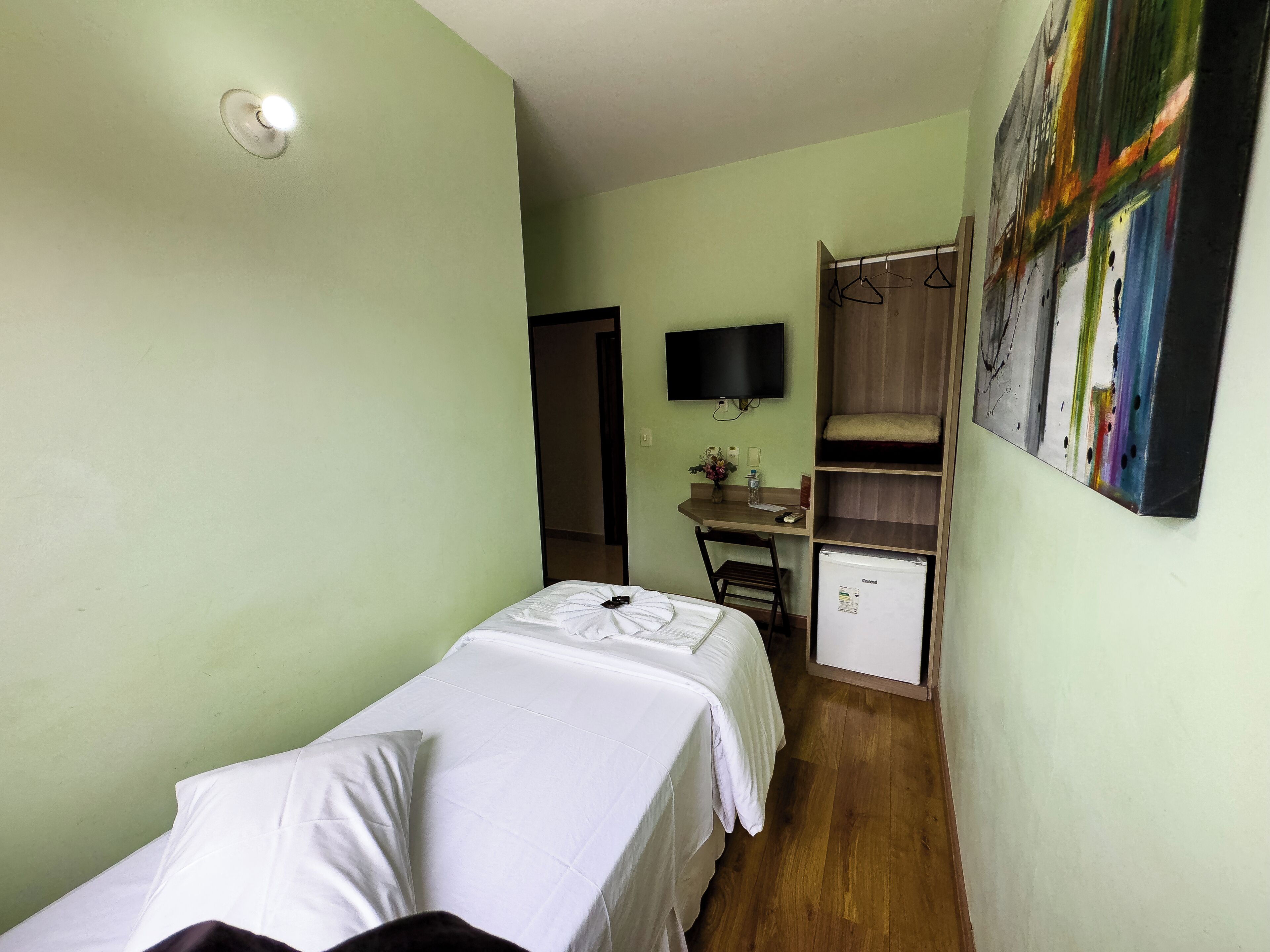 A small, clean room with a bed, a desk, a chair, a TV, and a refrigerator.