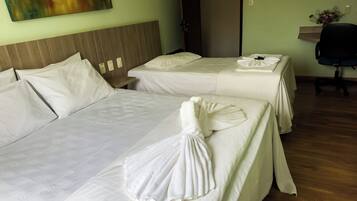 A hotel room with two beds, each with white linens and towels. There is a wooden headboard, a small table, and a chair. A painting is on the wall, and a vase with flowers is on a shelf.