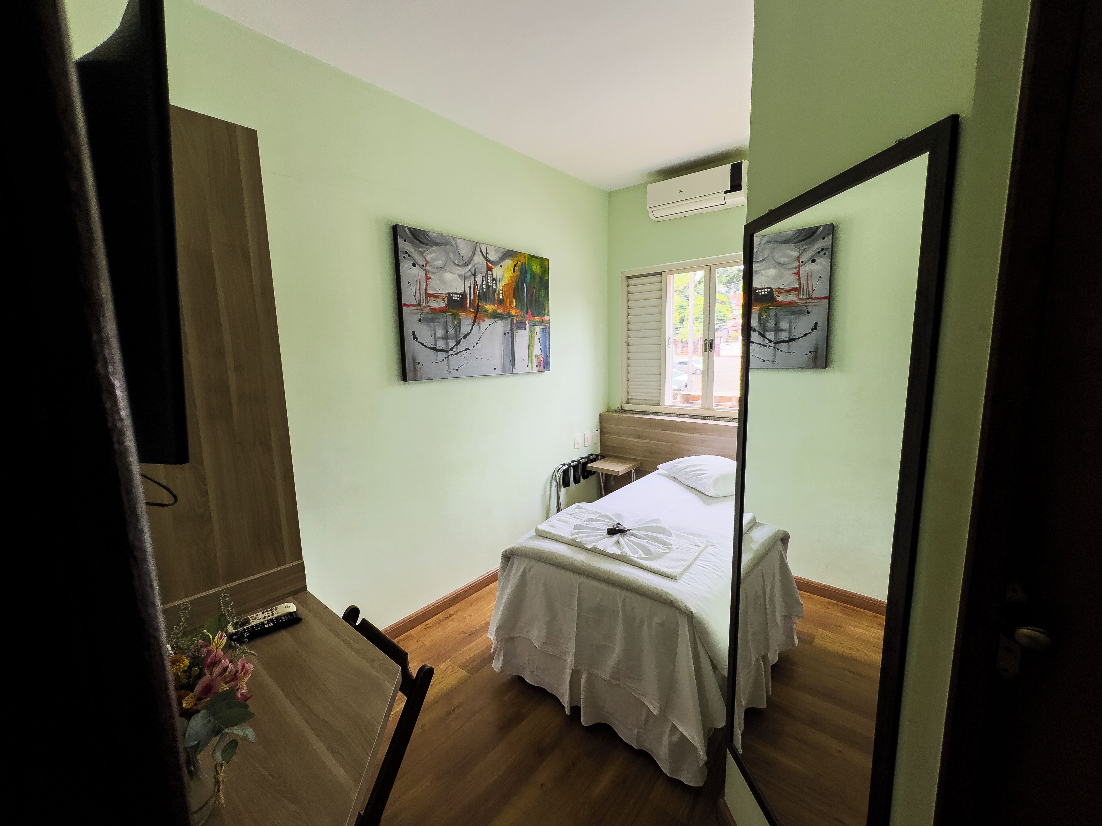 Un dormitorio con cama, escritorio y silla. Hay dos cuadros en la pared.