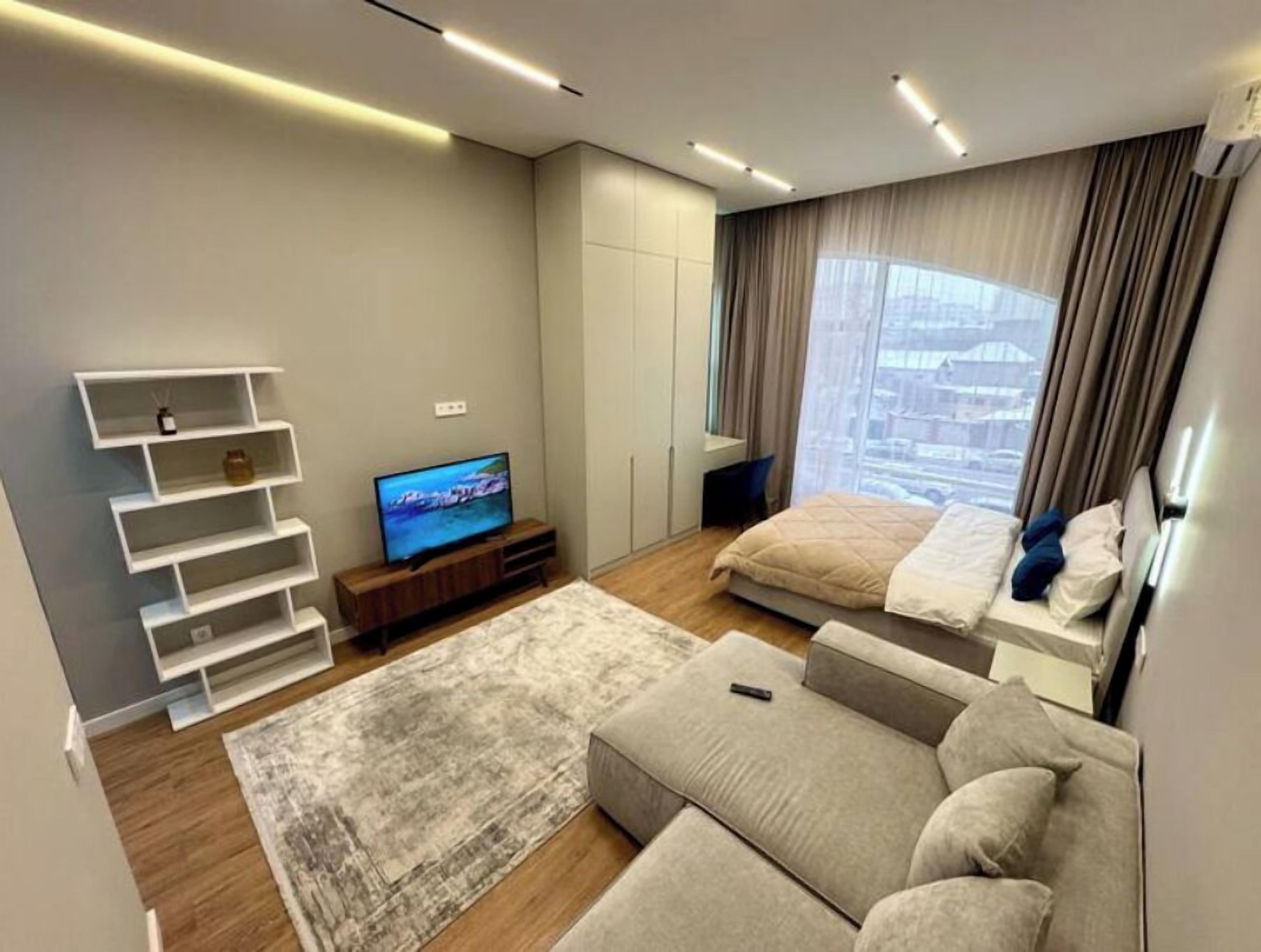 Ein modernes Schlafzimmer mit Bett, Fernseher, Sofa und einem Fenster mit Vorhängen.