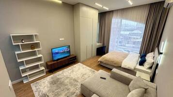 Ein modernes Schlafzimmer mit Bett, Fernseher, Sofa und einem Fenster mit Vorhängen.