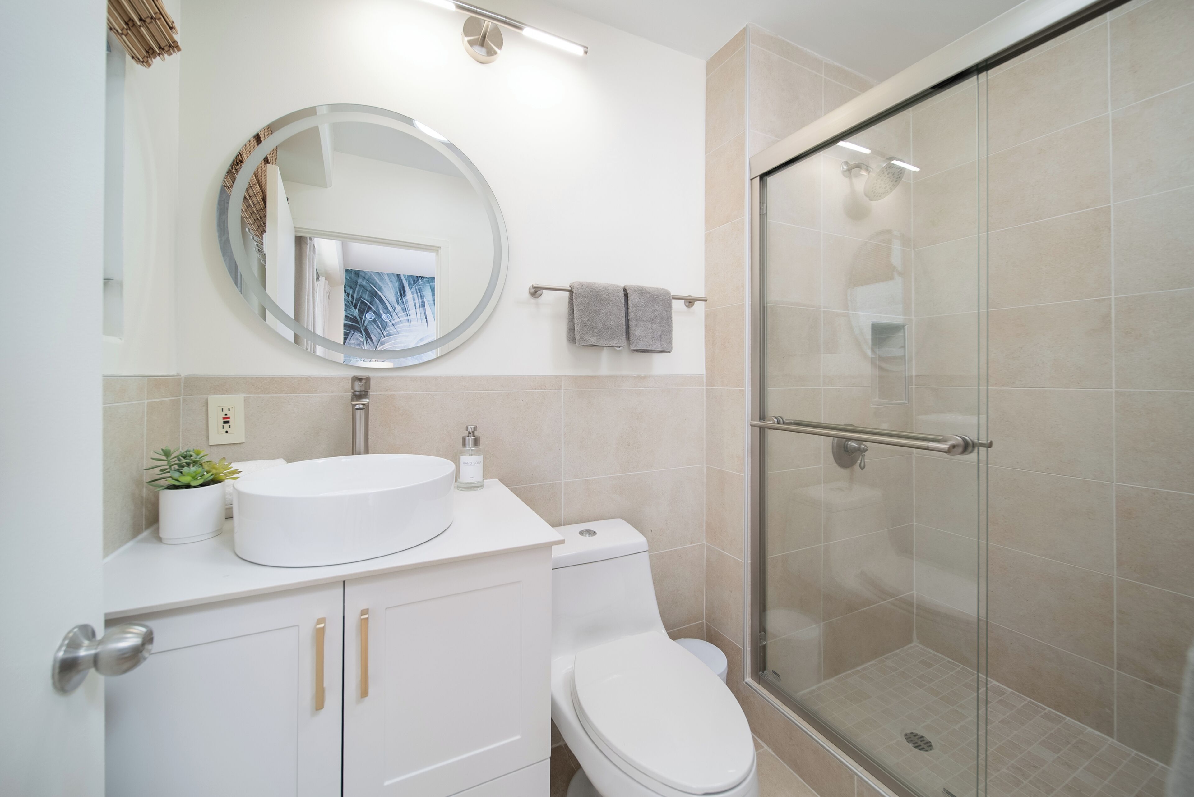 A modern bathroom with a round mirror, white sink, and a glass-enclosed shower.