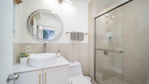 Un baño moderno con espejo redondo, lavabo blanco y ducha con mampara de vidrio.
