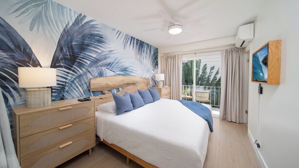 Un dormitorio con una cama grande, un aparador de madera, un ventilador de techo y vistas al exterior.