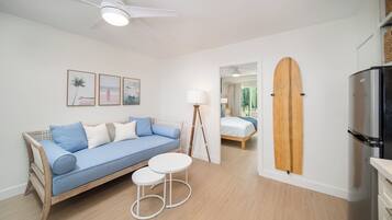 A modern living room with a blue sofa, white coffee table, and a surfboard mounted on the wall.