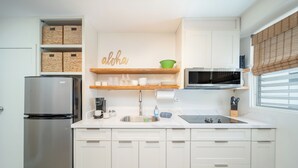 Una cocina moderna con armarios blancos, un refrigerador de acero inoxidable, un microondas y una estantería de madera con utensilios de cocina.