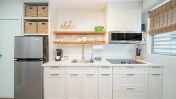 A modern kitchen with white cabinets, a stainless steel refrigerator, a microwave, and a wooden shelf with kitchen items.