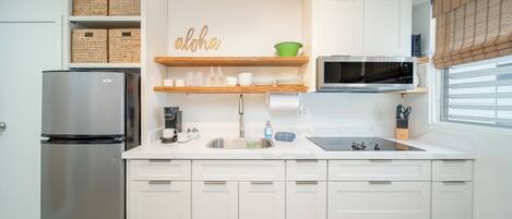 Une cuisine moderne avec des meubles blancs, un réfrigérateur en acier inoxydable, un four à micro-ondes et une étagère en bois où sont rangés des ustensiles de cuisine.