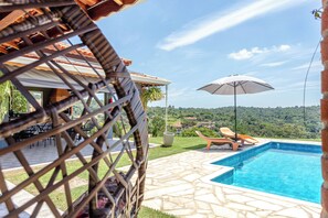 Zona de piscina con vistas al campo, mobiliario exterior y una pérgola.