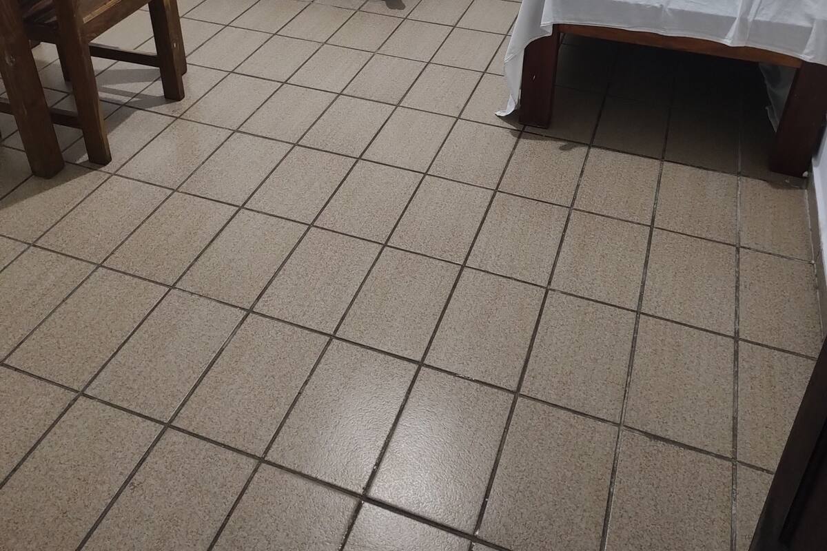 A small, clean room with two single beds, a wooden chair, and a small table.