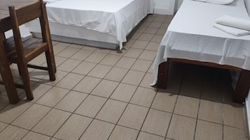 Quarto pequeno e limpo com duas camas de solteiro, uma cadeira de madeira e uma mesinha.
