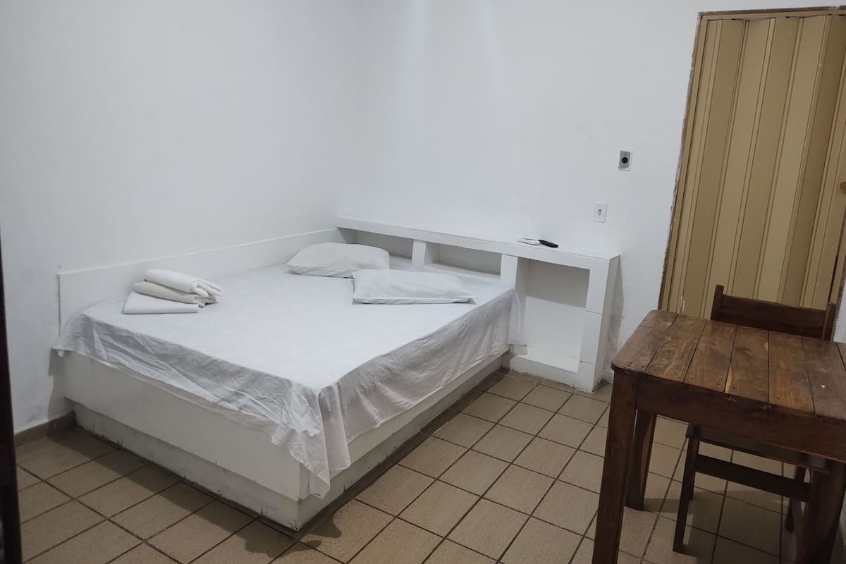 A small, clean room with a single bed, a wooden table, and a chair.