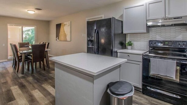 A modern kitchen with a central island, stainless steel appliances, and a dining area with chairs.