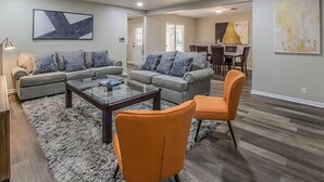 A spacious living room with a grey sofa set, a coffee table, and two orange chairs.