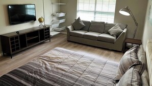 A modern living room with a sofa, a TV, a bookshelf, and a window with blinds.