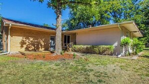A single-story house with a front porch, a small garden, and a tree in the yard.