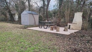 A picnic area with a table and benches, surrounded by trees and a shed.