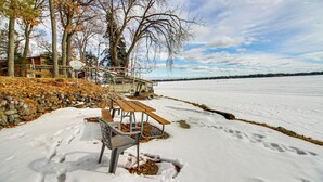 A snow-covered picnic area with benches and a picnic table, surrounded by trees and a stone wall. - Boat Dock & Fire Pit: Waterfront Home in Crosslake (Crosslake)