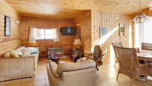 A cozy cabin interior with a sofa, a chair, a dining table, and a television mounted on the wall. - Boat Dock & Fire Pit: Waterfront Home in Crosslake (Crosslake)