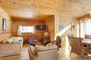 A cozy log cabin interior with a sofa, a chair, a dining table, and a television mounted on the wall. - Boat Dock & Fire Pit: Waterfront Home in Crosslake (Crosslake)