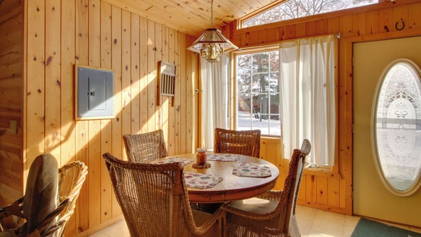 A wooden interior with a round dining table, wicker chairs, a chandelier, and a large window with curtains. - Boat Dock & Fire Pit: Waterfront Home in Crosslake (Crosslake)