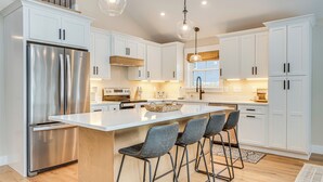 Una cocina moderna con armarios blancos, un refrigerador de acero inoxidable y taburetes de bar.