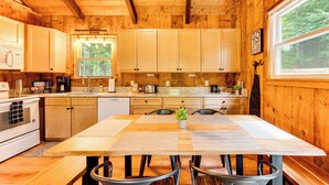A wooden cabin kitchen with a large dining table, wooden cabinets, and a view of the forest through a window. - 2 Mi to Conway: Cozy Cabin w/ Grill & Yard! (Center Conway)