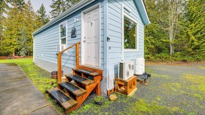 A small, light blue cabin with a front porch and steps, surrounded by a forest. - Remote Workers Welcome: Tiny Home in Port Angeles! (Port Angeles)