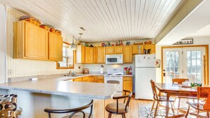 A kitchen with wooden cabinets, a central island with bar stools, a dining table, and a view of the outdoors through large windows. - 'Red Barn Getaway' Chillicothe Countryside Home (Chillicothe)