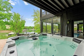 Un jacuzzi con vista a un lago y árboles, un porche cubierto y una piscina.