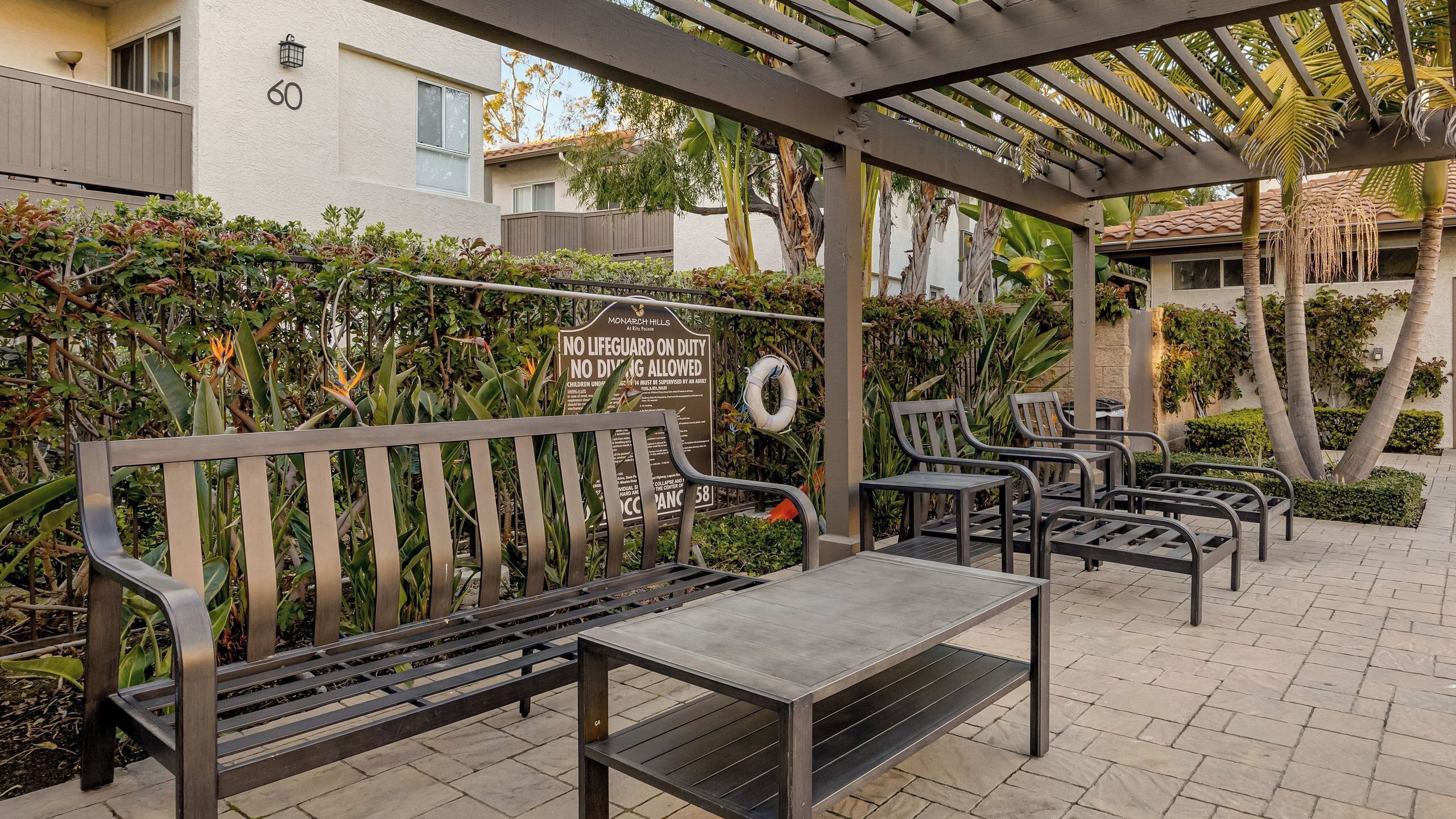 Un espace extérieur aménagé avec des bancs et des tables, entouré d’une végétation luxuriante et agrémenté d’une structure en forme de pergola.