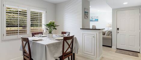 A dining area with a table set for four, a potted plant, and a view through the window.