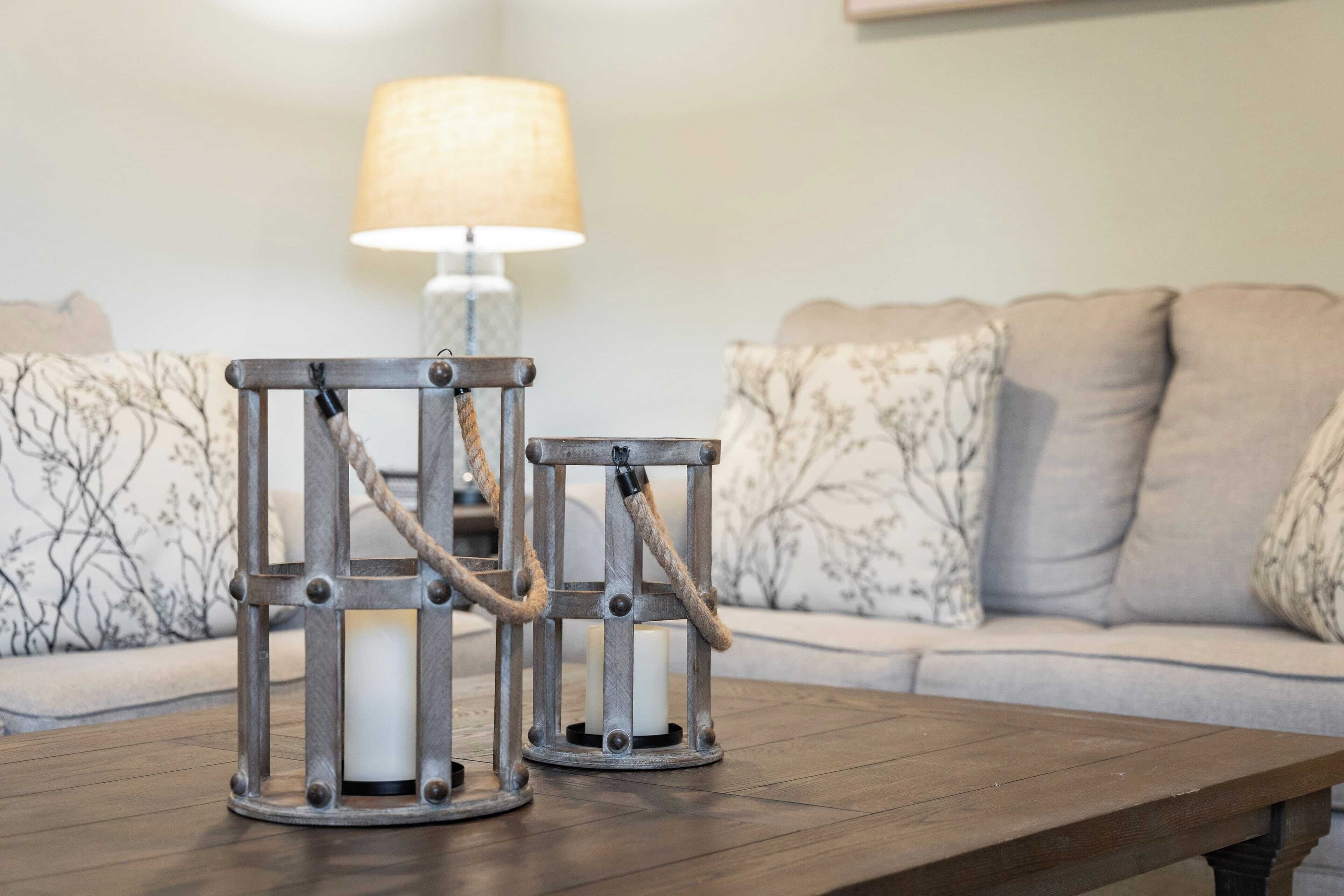 Two candle holders on a wooden table with a sofa and a lamp in the background.