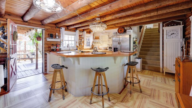 A rustic kitchen with wooden beams, a central island with stools, a chandelier, and a refrigerator. - < 4 Mi to Boat Ramp & Mickler Beach: Unique Cabin (Ponte Vedra Beach)