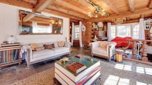 A log cabin interior with a white sofa, a coffee table with books, and a large mirror. - < 4 Mi to Boat Ramp & Mickler Beach: Unique Cabin (Ponte Vedra Beach)