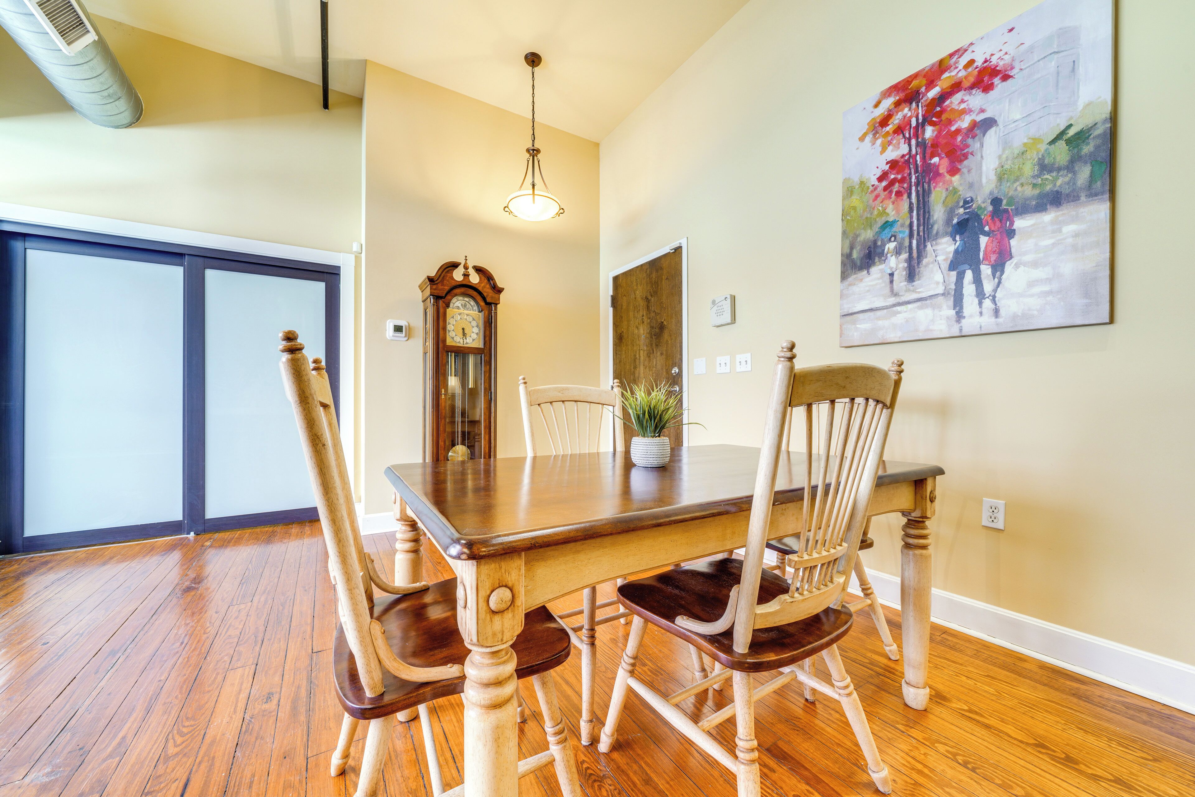 A dining area with a wooden table and chairs, a clock, and a painting on the wall.