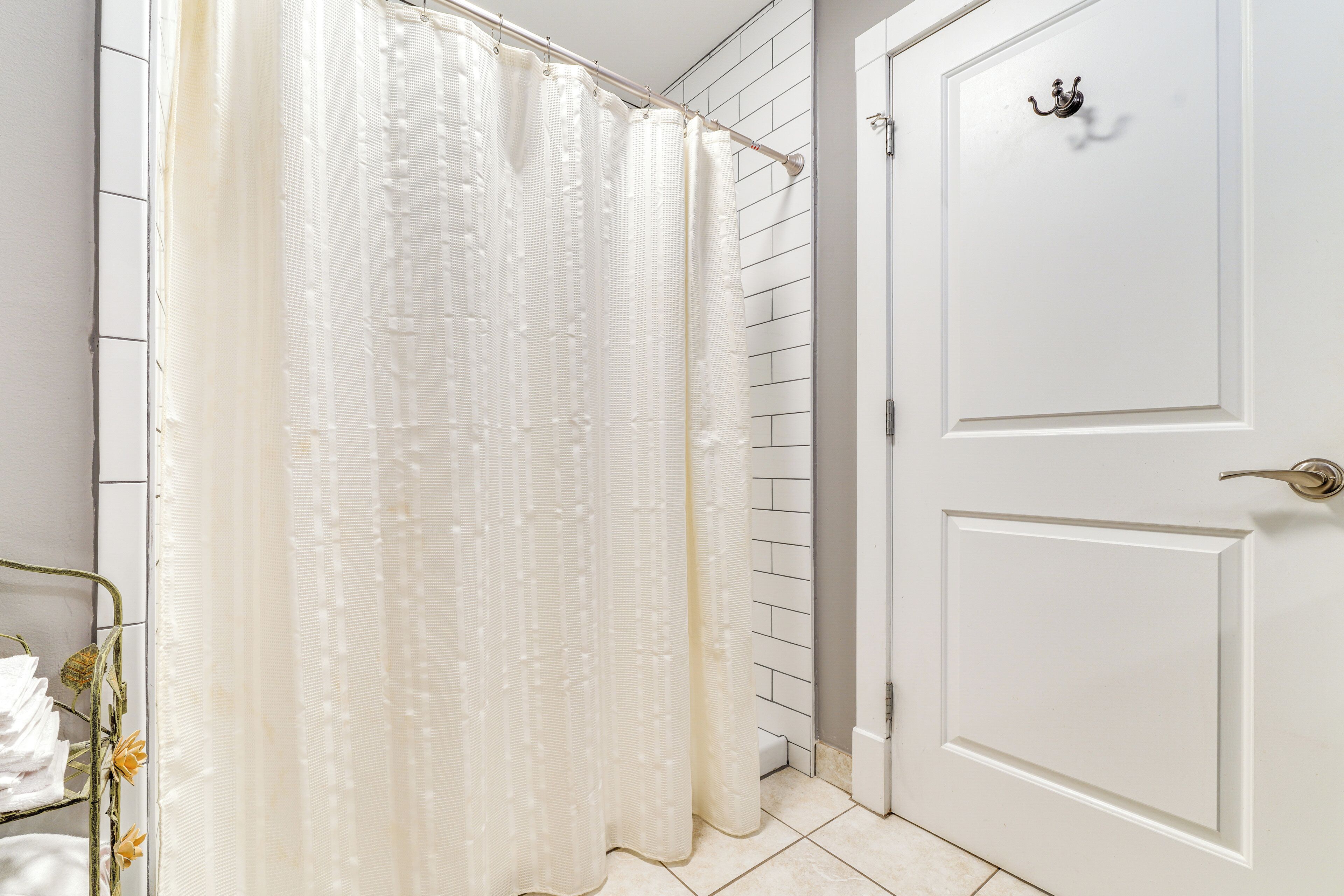 A bathroom with a white shower curtain, a white door with a brass handle, and a metal rack with folded towels.