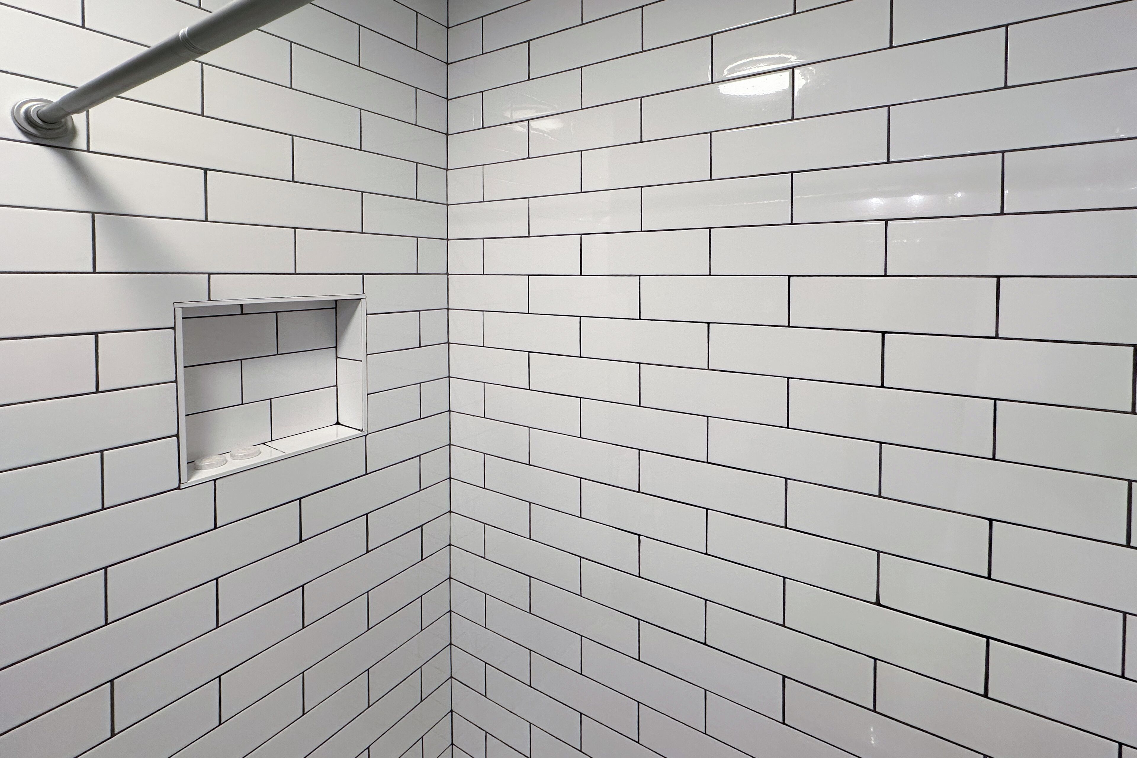 A corner of a room with white tiled walls and a metal towel rack.