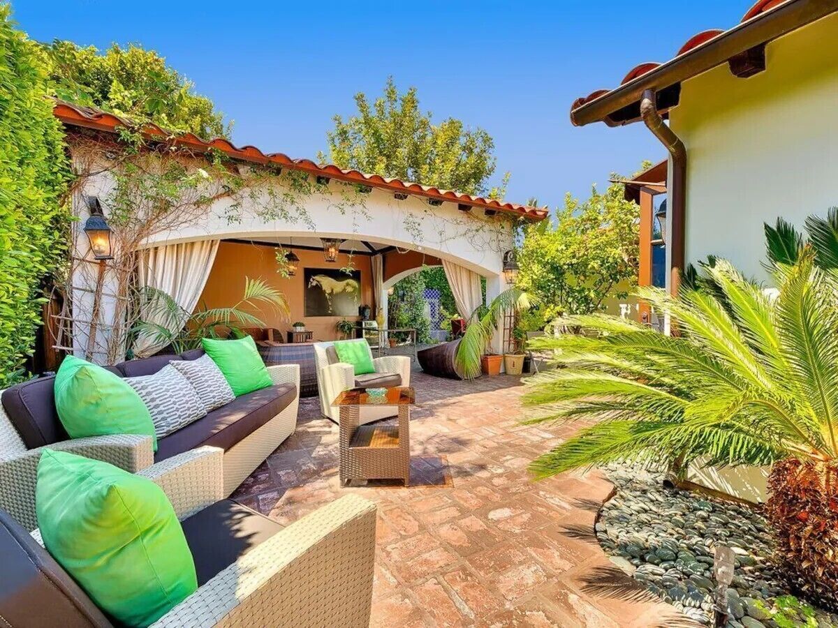 Un patio exterior con mobiliario de mimbre, una zona de estar cubierta y una palmera.