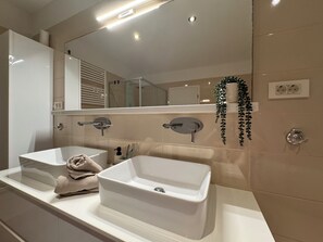 A modern bathroom with two sinks, a large mirror, and a shower.