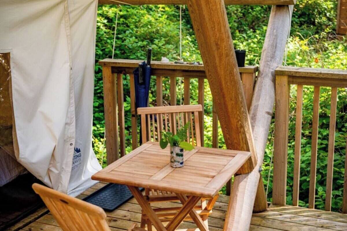 A wooden deck with a table and chairs, a tent, and a wooden railing.