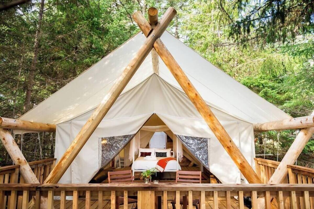 A tent with a bed, wooden railings, and a table with a vase.