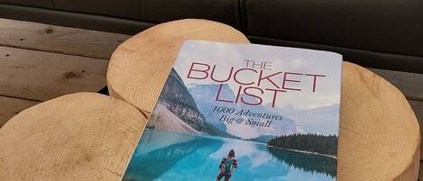 Un sofá de cuero con una manta de piel, un libro titulado 'The Bucket List' sobre un taburete de madera y una mesa de madera.