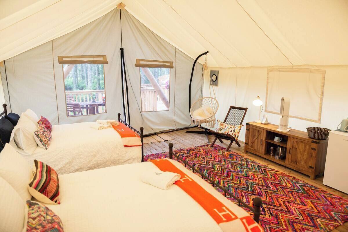 A tent with two beds, a hanging chair, a desk with a lamp, and a view of the outdoors.