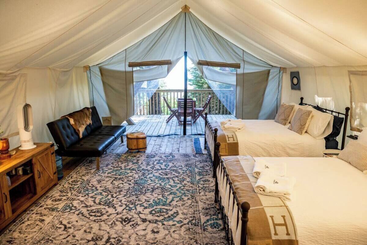 A tented accommodation with a bed, a sofa, a small table, and a chair.