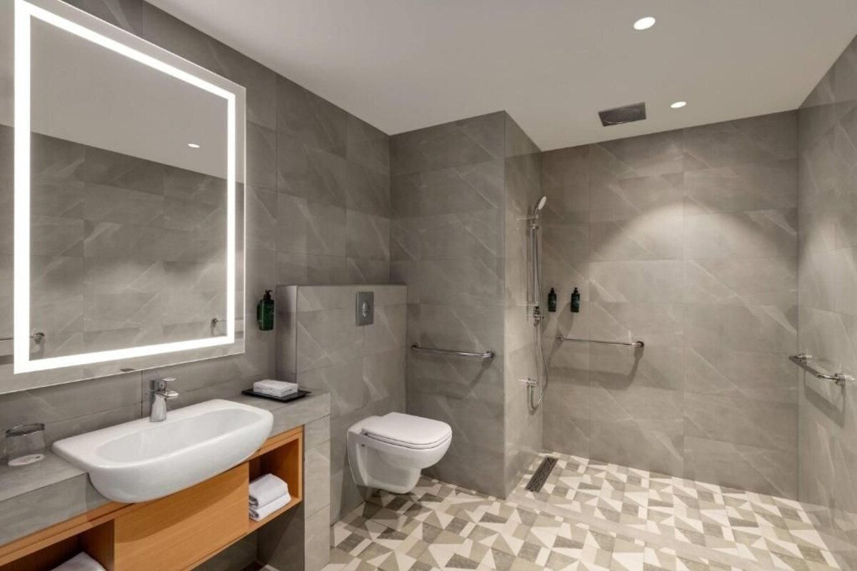 Un baño moderno con un espejo grande, un lavabo, un inodoro y una ducha.