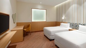 A hotel room with two single beds, a desk, a chair, a TV, and a window with frosted glass.