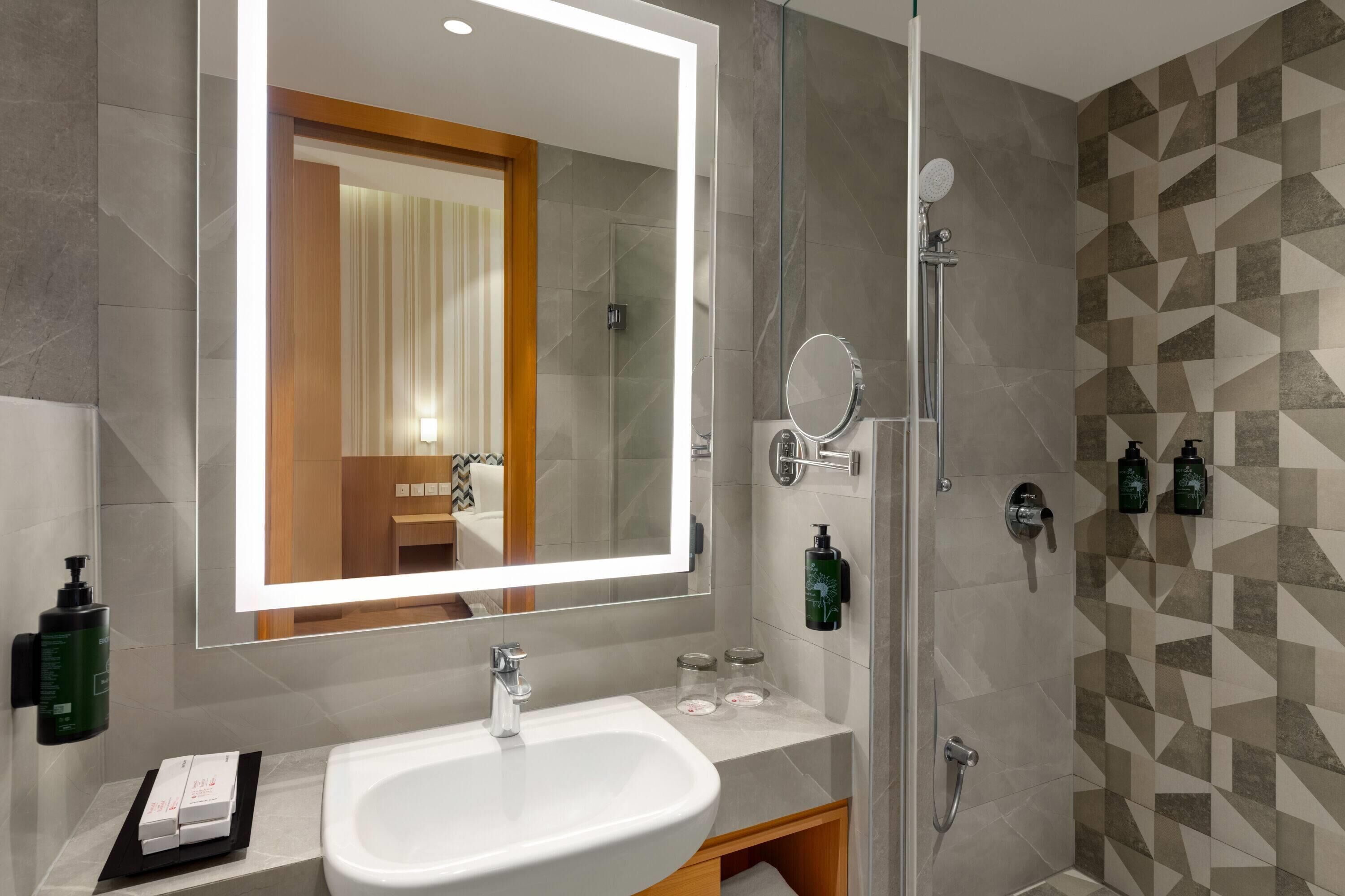 A modern bathroom with a large mirror, a sink, and a shower.